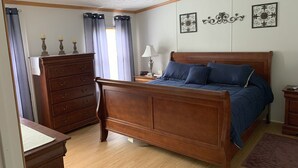 Quarto com cama de madeira, penteadeira, mesa de cabeceira e abajur.