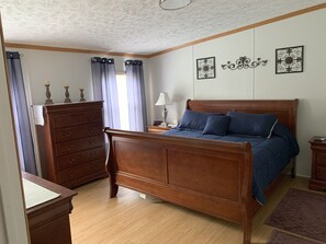 A bedroom with a wooden bed, a dresser, a nightstand, and a lamp.