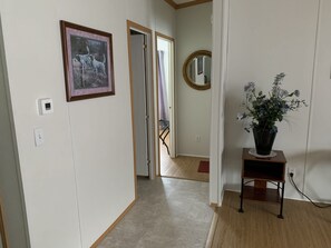 A hallway with a framed picture, a thermostat, a mirror, and a potted plant on a small table.
