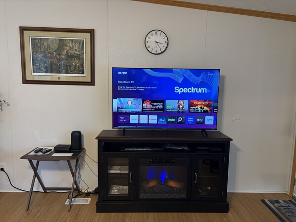 Un televisor sobre un soporte, una pantalla digital, un reloj en la pared y un cuadro enmarcado encima.