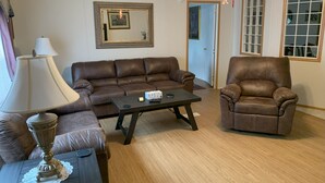 Uma sala de estar com sofá de couro marrom, poltrona combinando, mesa de centro e abajur.