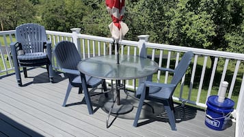 A deck with a round glass table and four chairs, surrounded by a white railing.