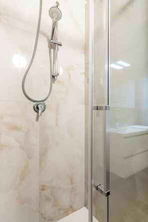 A modern bathroom with a glass shower enclosure, a handheld showerhead, and a wall-mounted faucet.
