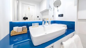 Ein modernes Badezimmer mit einem großen weißen Waschbecken, einer blauen Arbeitsplatte und einem Spiegel darüber. Auf der Arbeitsplatte stehen Pflegeprodukte und darunter befindet sich ein Handtuchhalter.