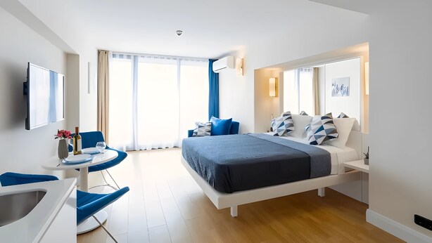 Ein modernes Hotelzimmer mit einem großen Bett, einem Schreibtisch mit Stuhl, einem Flachbildfernseher und einem Fenster mit Vorhängen.