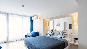 Ein modernes Hotelzimmer mit einem großen Bett, einem Nachttisch, einem Schreibtisch und einem großen Fenster mit Vorhängen.