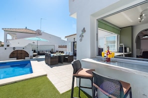 A pool, outdoor seating, and a bar area with a view of the house.