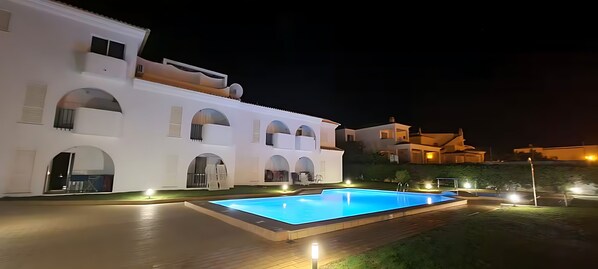 A white villa with a swimming pool and outdoor lighting.
