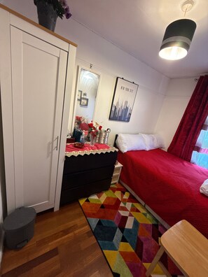 Un dormitorio con cama, cómoda, espejo, alfombra colorida y un cartel en la pared.