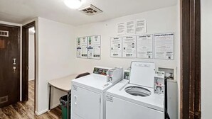 Une buanderie équipée d’un lave-linge et d’un sèche-linge, d’une poubelle et de panneaux d’information accrochés au mur.