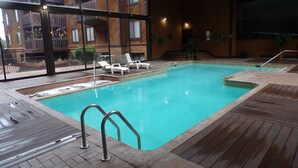 Une piscine avec une terrasse en bois, des chaises longues et une vue sur un immeuble doté de balcons.