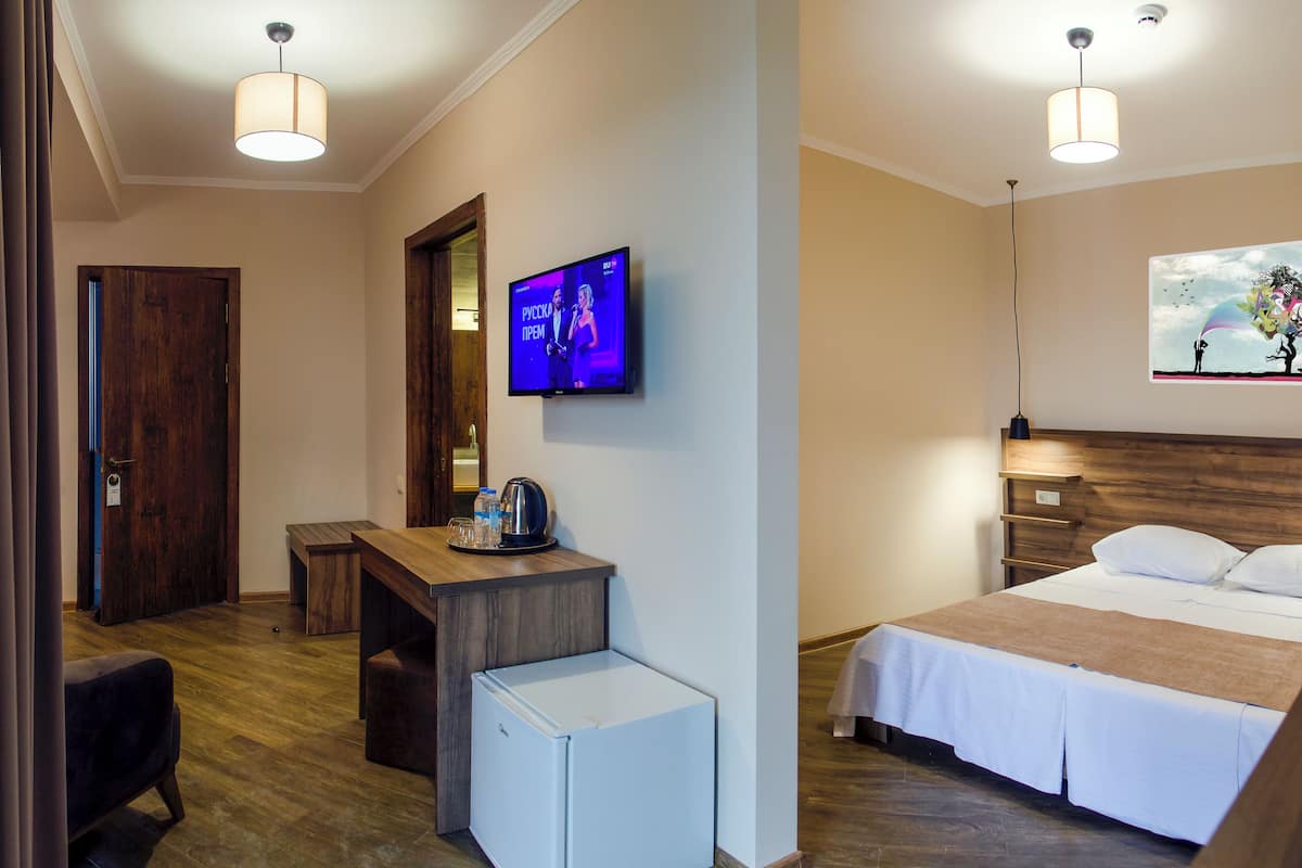 Habitación de hotel con cama, escritorio, refrigerador pequeño, televisión y un cuadro en la pared.