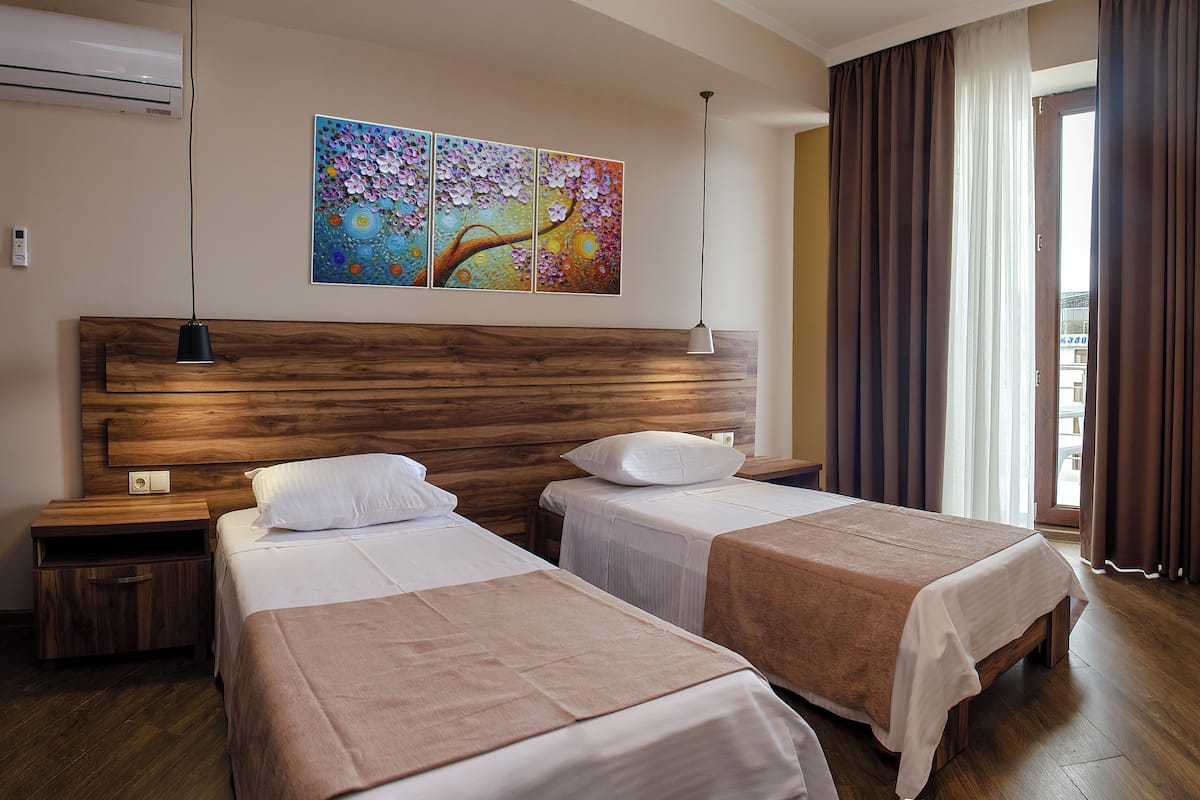 Habitación de hotel con dos camas, cabecero de madera, un cuadro en la pared y una ventana con cortinas.