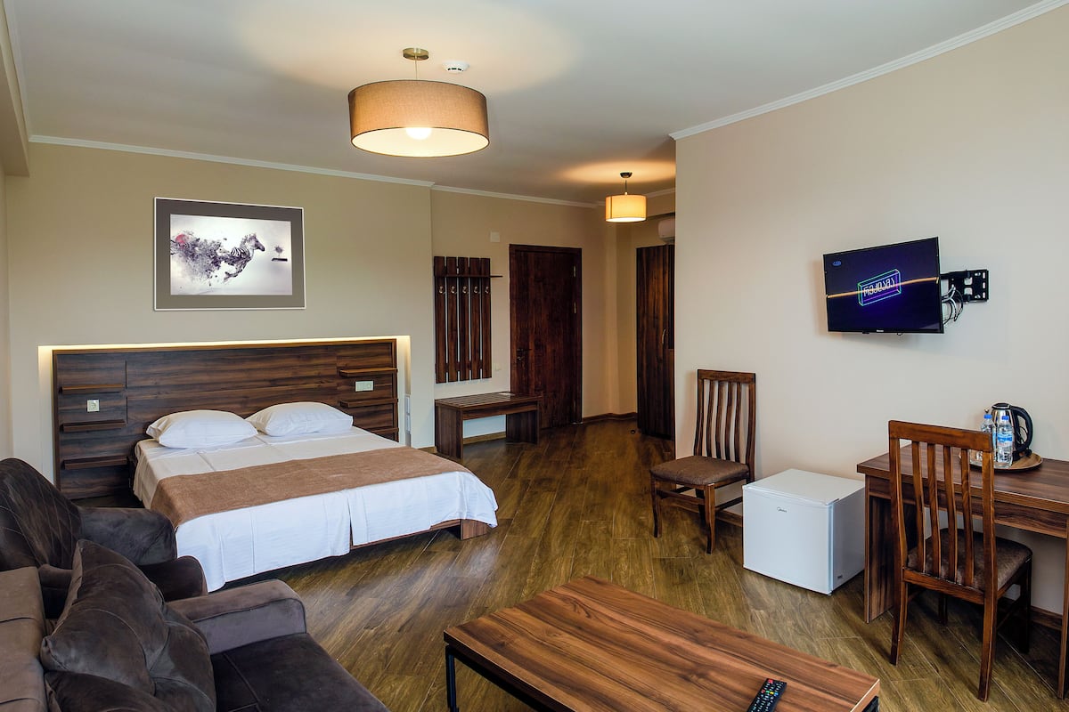 Una habitación de hotel con cama, sofá, escritorio, silla, televisor y refrigerador.
