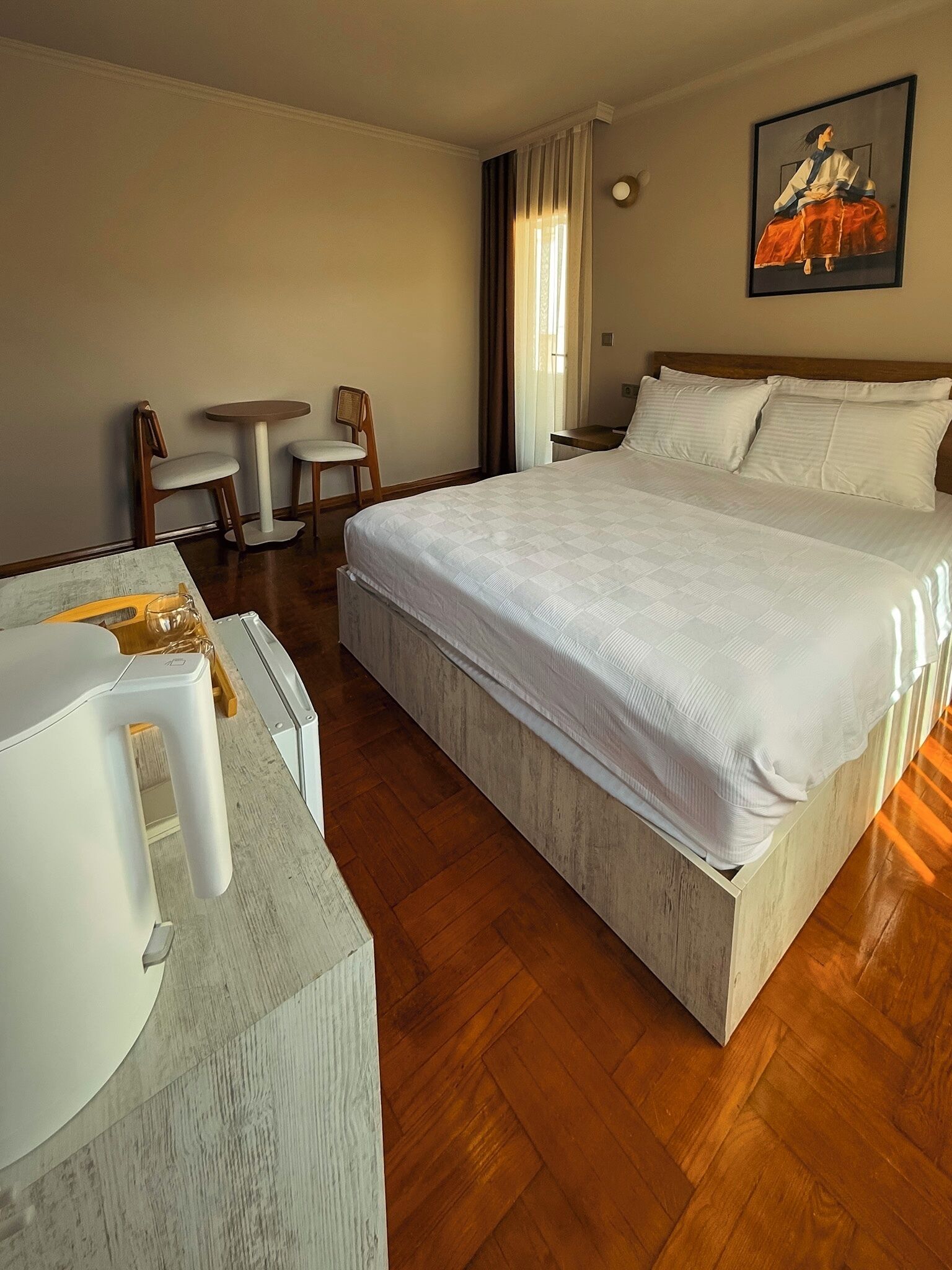 Une chambre d’hôtel avec un grand lit, un bureau avec une chaise, une petite table et un tableau au mur.