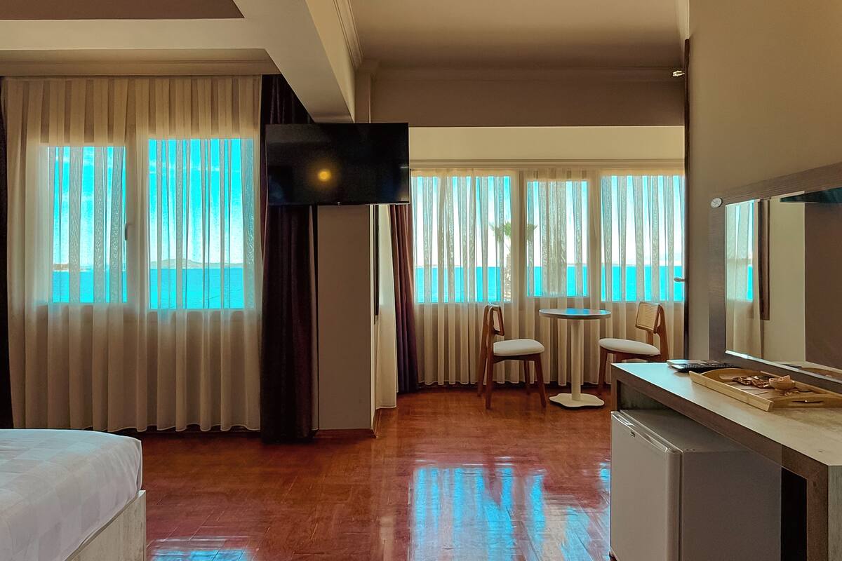 Ein Hotelzimmer mit Bett, Schreibtisch, Stuhl, Fernseher und großen Fenstern mit Vorhängen.