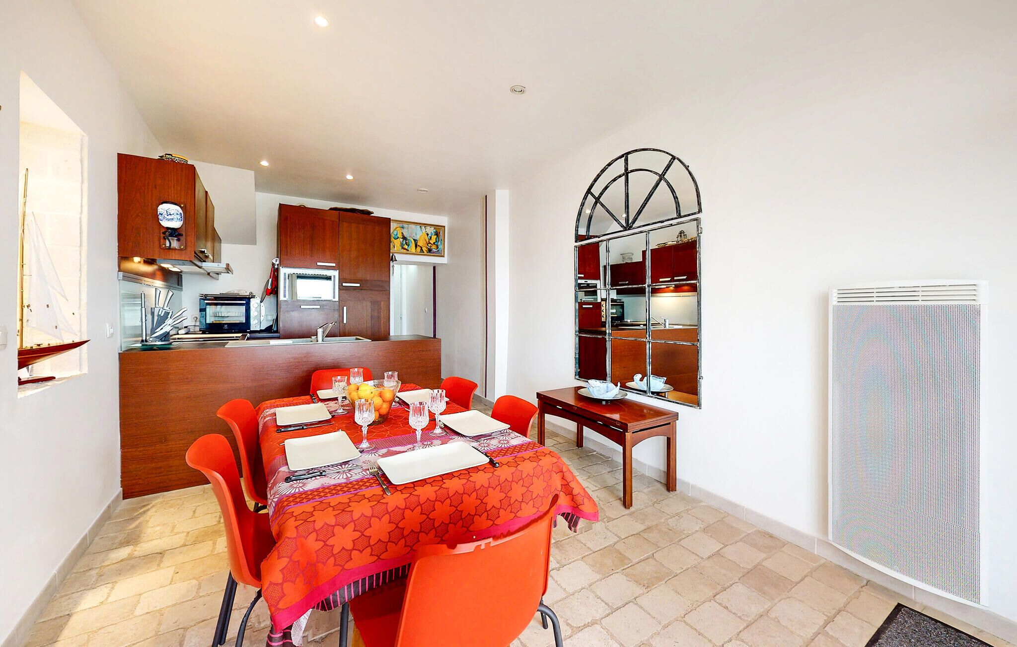 A dining area with a table set for four, a kitchen in the background, and a large mirror with a red frame.