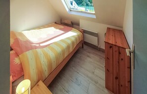 Ett litet rum med en enkel säng, ett sluttande tak och ett takfönster, trägolv, ett litet bord vid sängen med en lampa och ett litet träskåp.