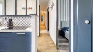 Een moderne keuken met een gekleurde spatwand, een houten vloer en een gang die leidt naar een slaapkamer met een gestreept behang en een bed.