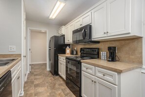 A kitchen with white cabinets, a black refrigerator, a microwave, a stove, and a coffee maker.