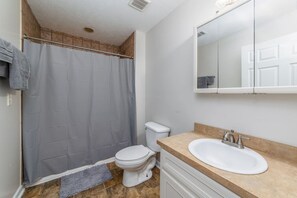 A bathroom with a shower curtain, toilet, sink, and a mirror above the sink. - Budget 1BR Near Ft. Moore & Airport w. HDTV & WiFi (Columbus)