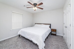A bedroom with a bed, a nightstand, a ceiling fan, a window with blinds, and a door. - Budget 1BR Near Ft. Moore & Airport w. HDTV & WiFi (Columbus)