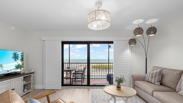A modern living room with a TV, sofa, chairs, and a balcony with a view of the beach.