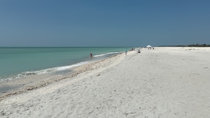 A wide sandy beach with clear turquoise water and a few people walking along the shore.