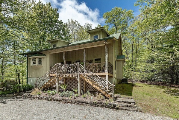 A wooden cabin with a porch and a staircase made of branches, surrounded by trees.