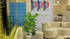 Un soggiorno moderno con un divano beige, un tavolino da caffè, una grande pianta in vaso e una TV a parete.