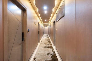 Un couloir d’hôtel avec des portes en bois, une moquette à motifs et des luminaires encastrés.