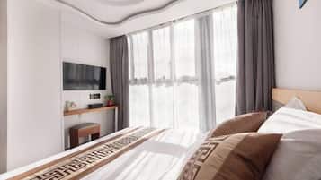 Quarto de hotel moderno com uma cama grande, uma escrivaninha com computador e uma janela com cortinas.