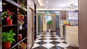 Een hotel receptie met een incheckbalie, een zwart-wit geruit vloertapijt en potplanten op planken.