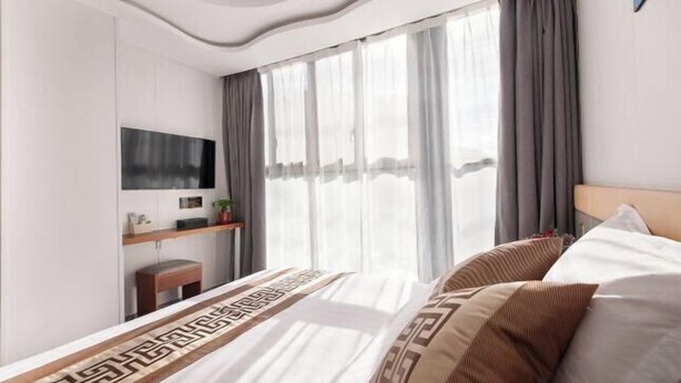 Een moderne hotelkamer met een groot bed, een flatscreen televisie aan de muur, een klein bureau met een stoel en een groot raam met gordijnen.