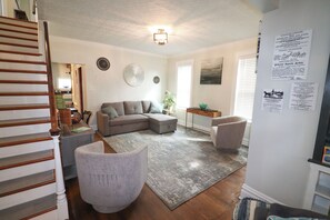 Ein Wohnzimmer mit Ecksofa, grauem Sessel, einem kleinen Tisch und einer Treppe.