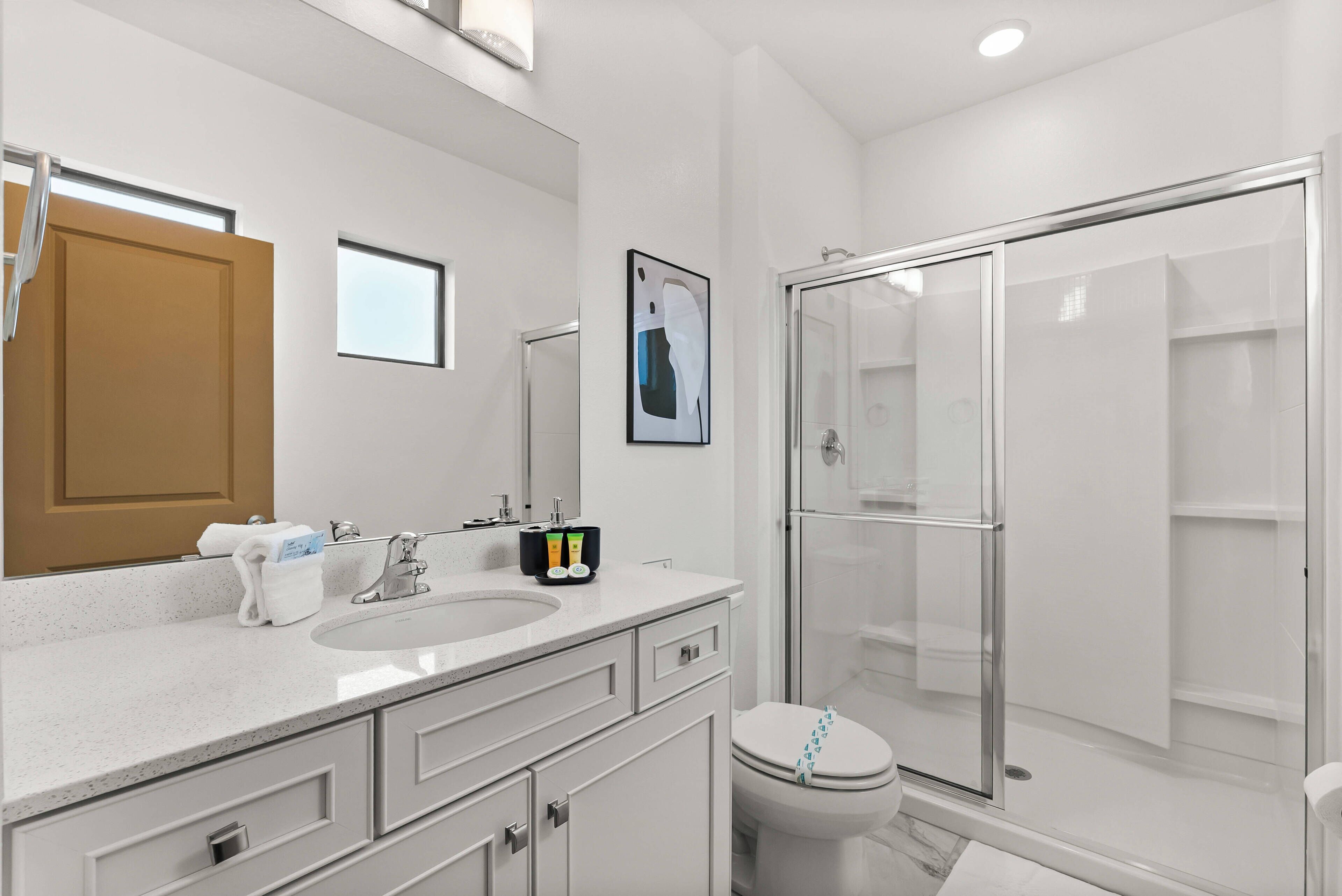 Un baño moderno con un espejo grande, un lavamanos, un inodoro y una ducha con mampara de vidrio.