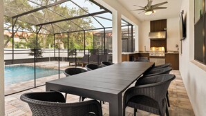 Un espace extérieur aménagé pour les repas, avec une piscine, une terrasse couverte et un coin cuisine.