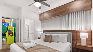 Une chambre d’hôtel moderne avec un grand lit, une tête de lit en bois, un ventilateur de plafond et une table de chevet avec une lampe.