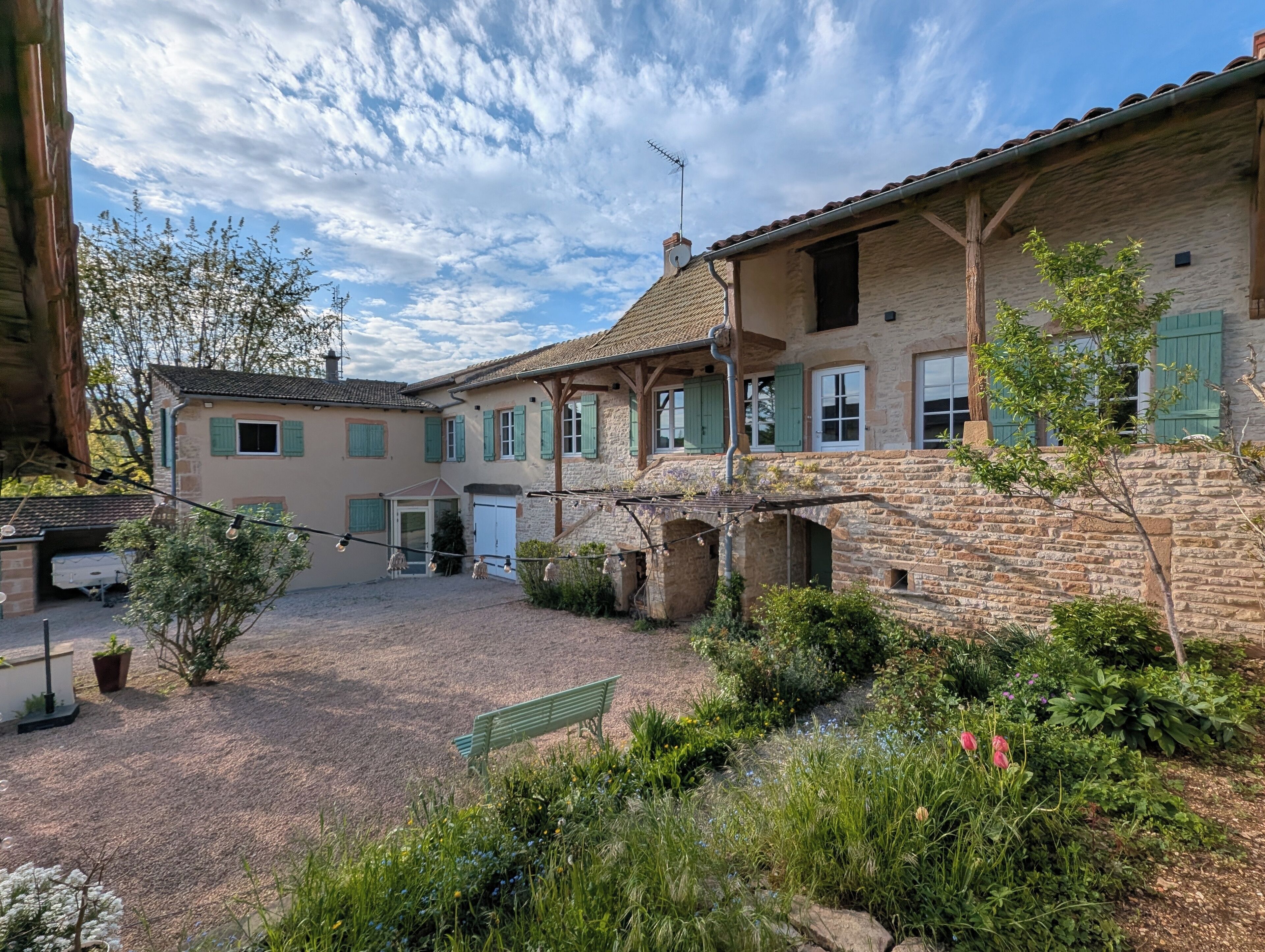 A traditional stone building with a courtyard, featuring a bench and potted plants.