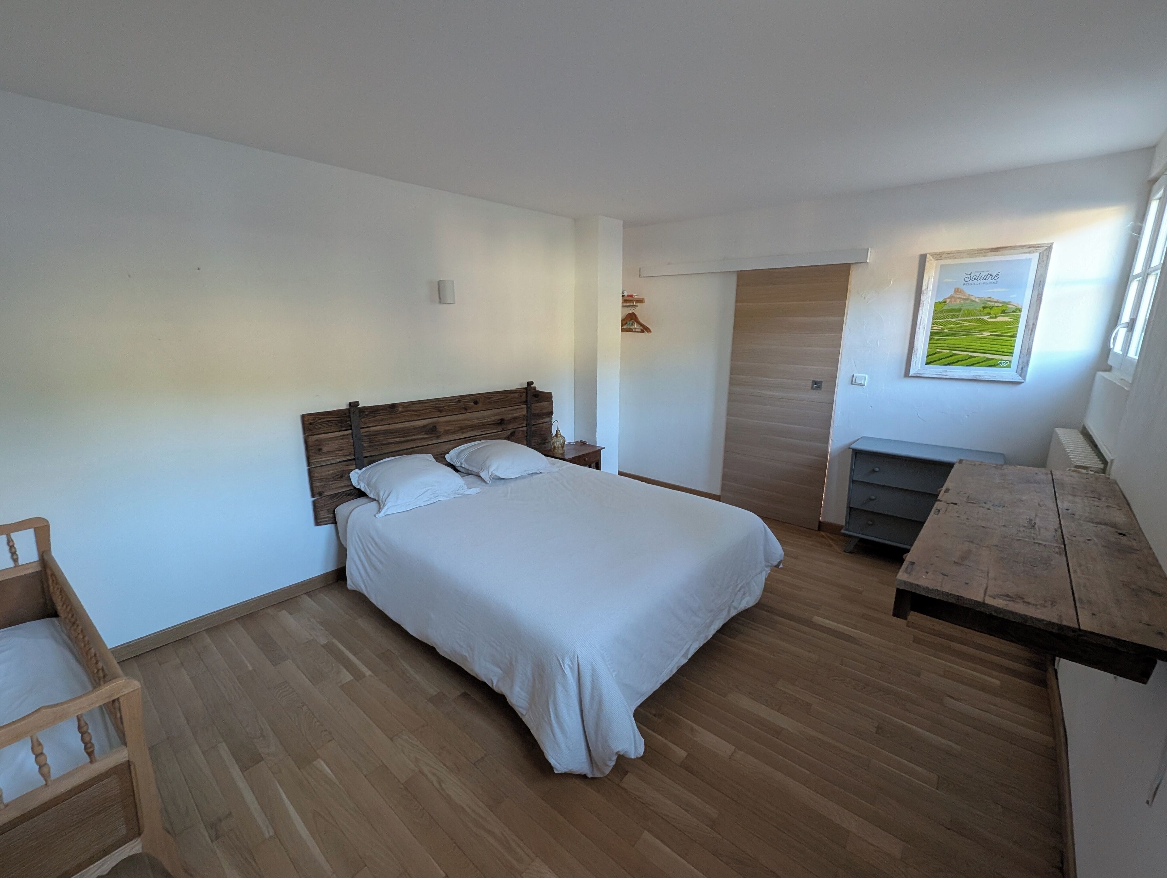 Un dormitorio con una cama de madera, una mesita de noche de madera, un banco de madera y un cuadro enmarcado en la pared.