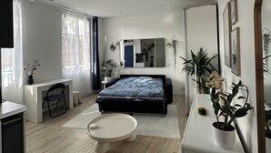 A modern bedroom with a bed, bedside table, desk, chair, and potted plants. - Studio Bassin de la Villette (Paris)