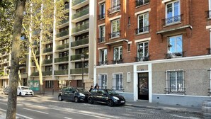 A multi-story residential building with balconies, a paved street, and parked cars. - Studio Bassin de la Villette (Paris)