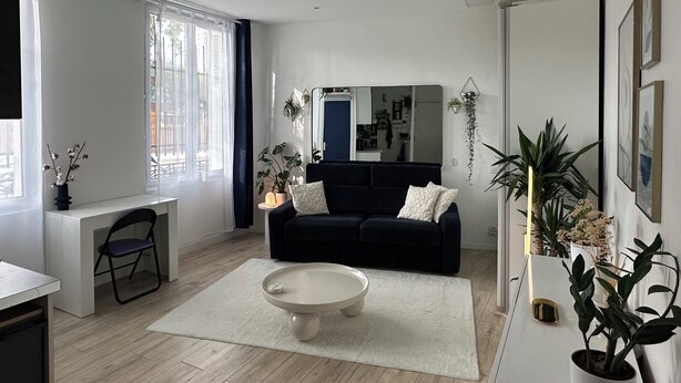 A modern living room with a dark blue sofa, a white coffee table, and a large window with sheer curtains. - Studio Bassin de la Villette (Paris)