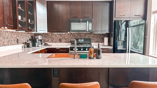 Une cuisine moderne avec des meubles de couleur bois foncé, un grand îlot central doté de tabourets, un four à micro-ondes encastré et un réfrigérateur.