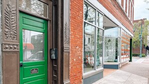 Une porte verte avec une pancarte indiquant « Il est interdit de s’attarder », un bâtiment en briques et de grandes fenêtres.