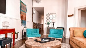 Un salon avec deux fauteuils turquoise, une table basse ronde, un fauteuil rouge et un canapé marron.