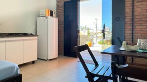 A compact kitchen with a refrigerator, a dining table with chairs, and a view through a glass door to an outdoor area. - Pousada Aracuã - Laguna (Laguna)