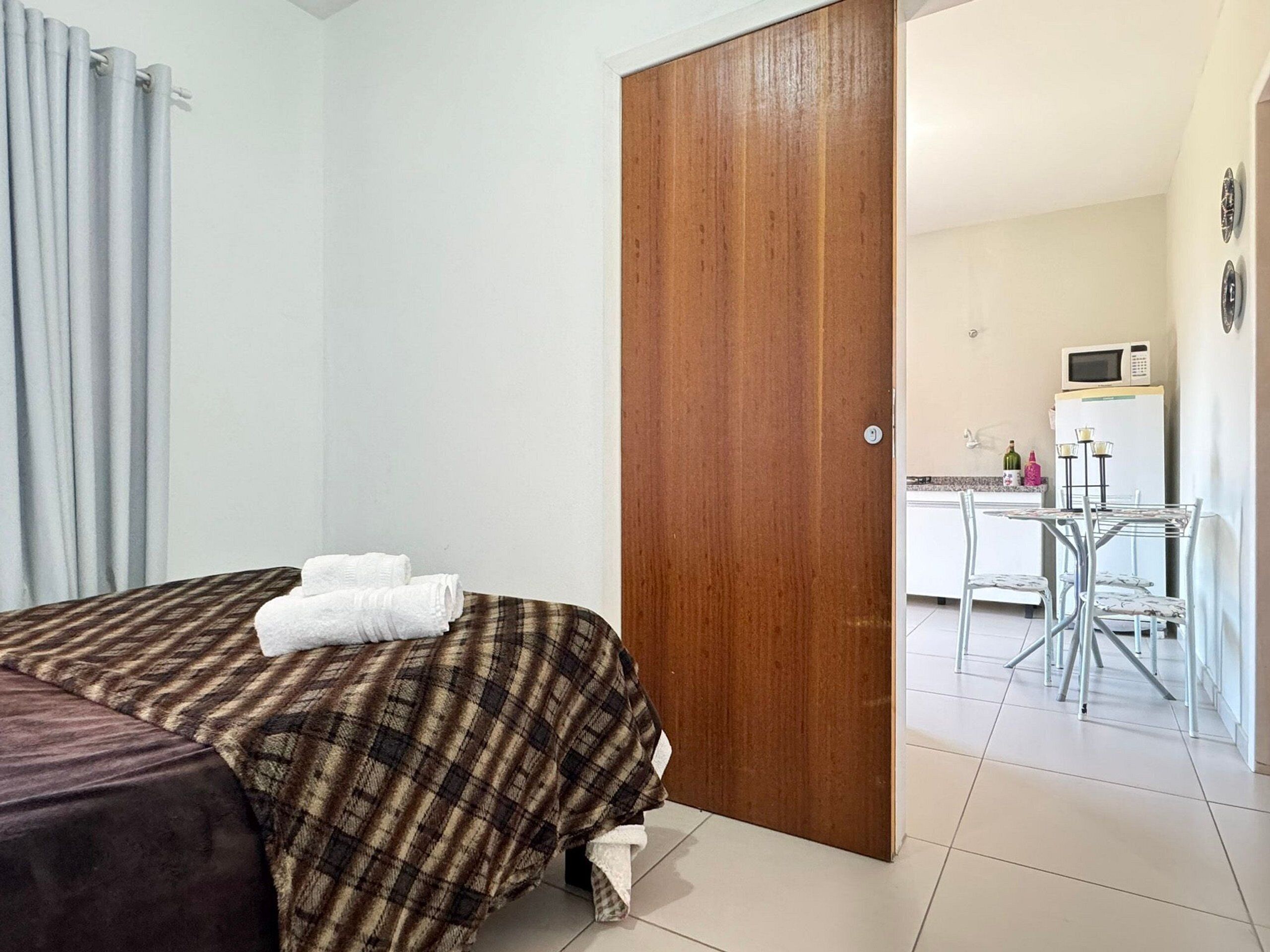 A hotel room with a bed, a wooden door, a kitchenette, and a dining area.