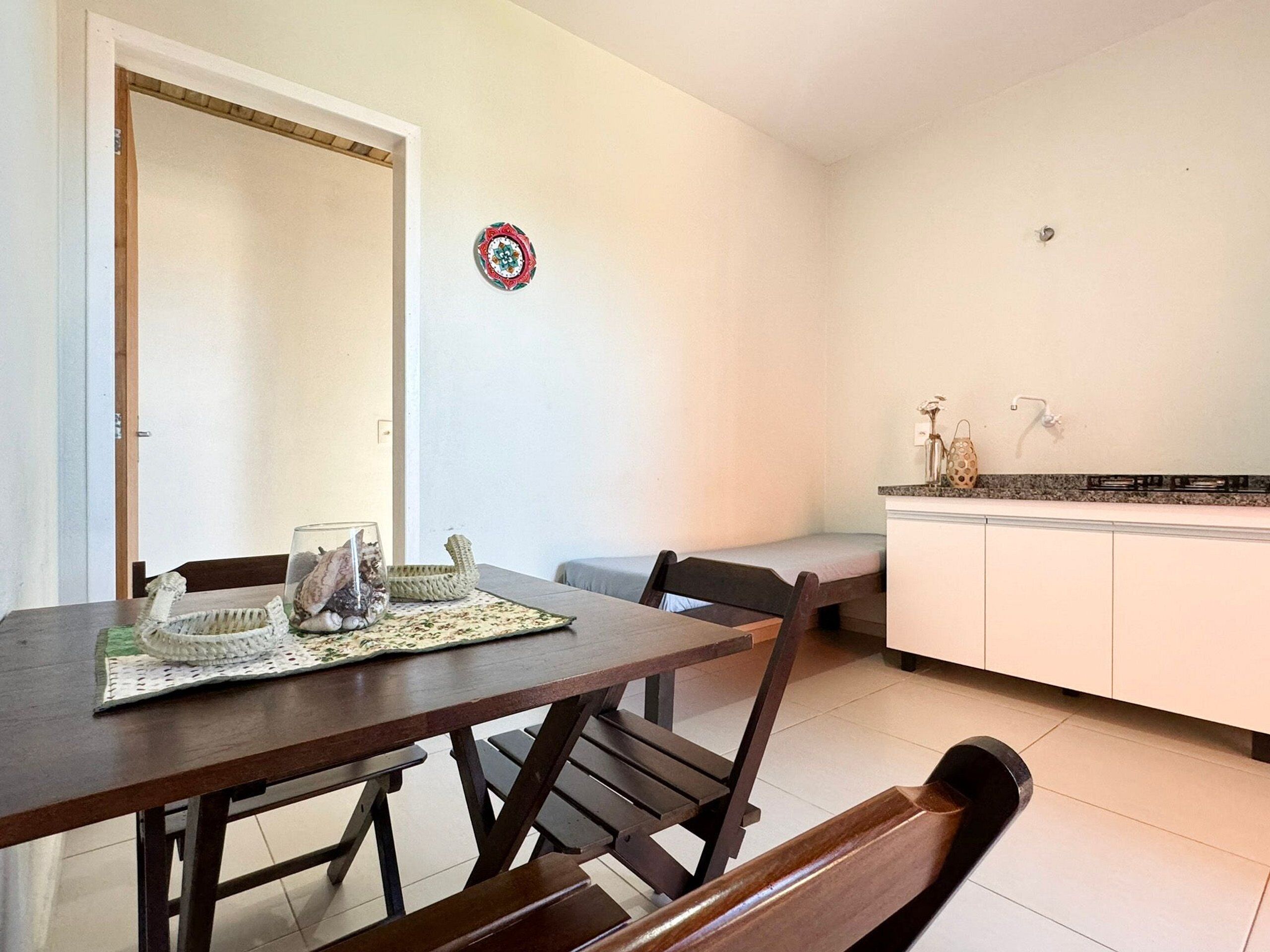 A dining area with a wooden table, chairs, and a bench. There is a kitchen area with a sink and cabinets.