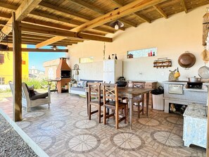 Una cucina esterna rustica con un forno a mattoni, mobili in legno e pavimento piastrellato.